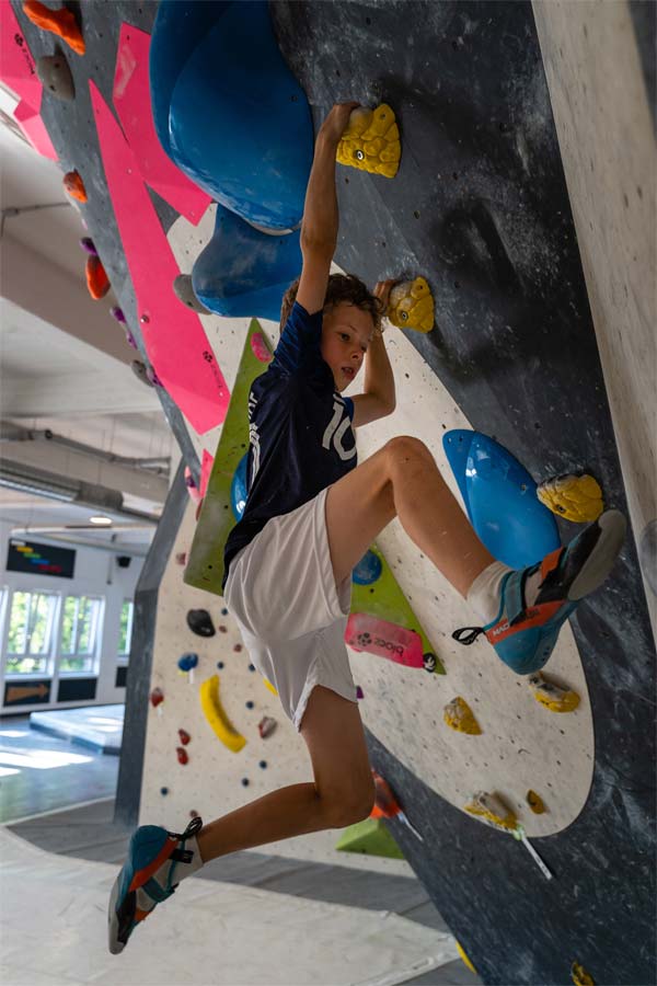 Junge hält sich an zwei gelben Griffen an der Boulderwand fest