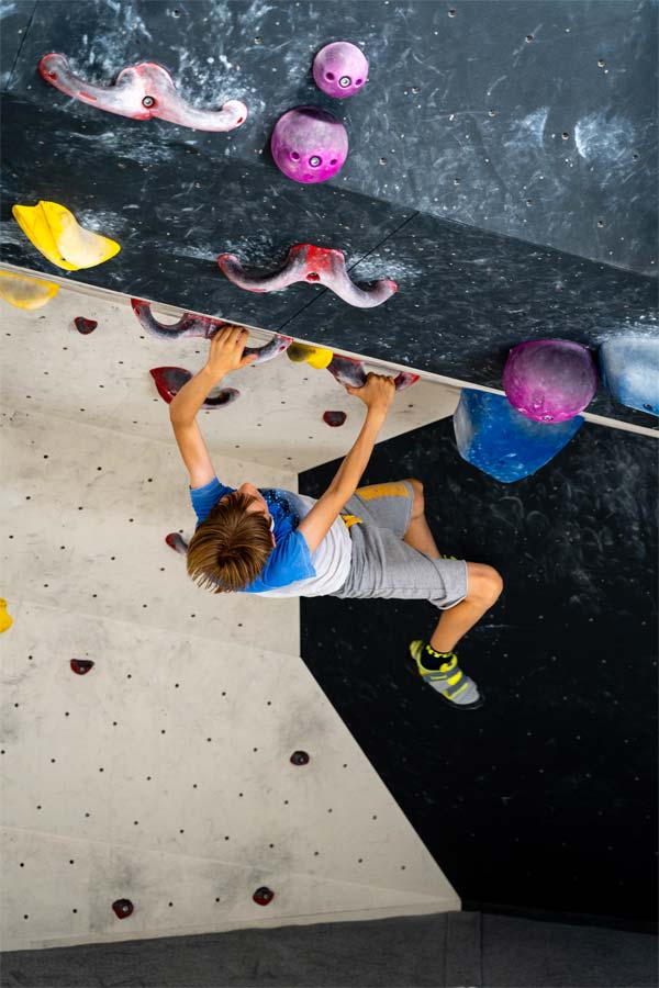 Junge hält sich an zwei roten Griffen an der Boulderwand fest