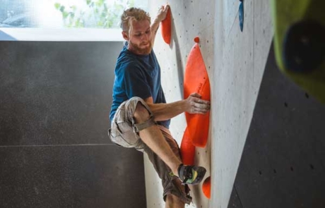 urban apes Hamburg Ost Mann an der Boulderwand vor einem Fenster