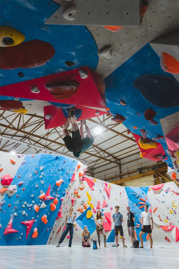 Boulderer am Überhang. Im Hintergrund steht eine Gruppe von Freunden.