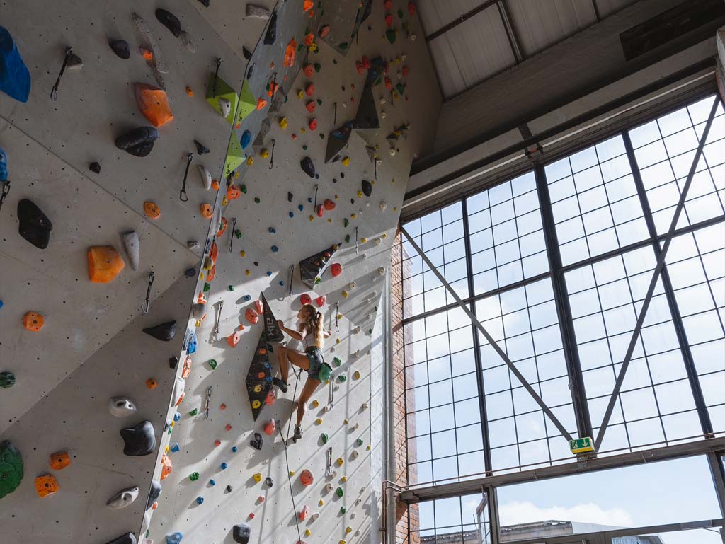 Kletterin beim Vorstiegsklettern vor einem großen Fenster.