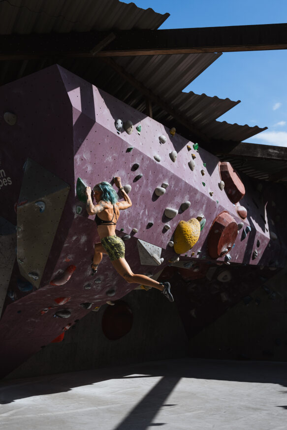 Boulderin beim Sprung an einer violetten Boulderwand im Aussenbereich vom urban apes Bright Site