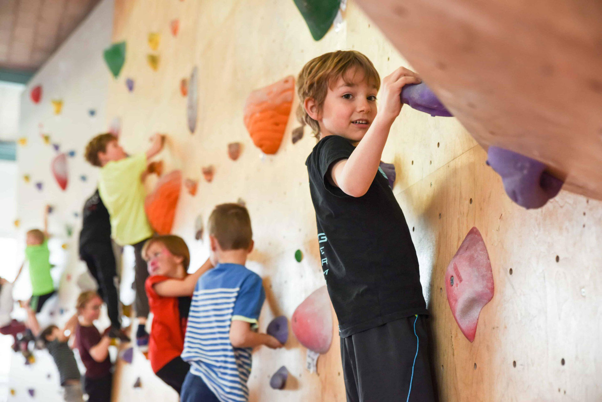 Kinder sind an der Boulderwand im urban apes Bright Site. Junge in Vordergrund hält sich an lila Griff fest.