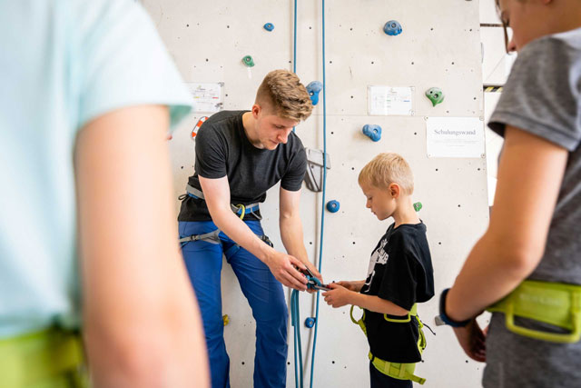 Trainer zeigt Kindern das Sichern beim Klettern