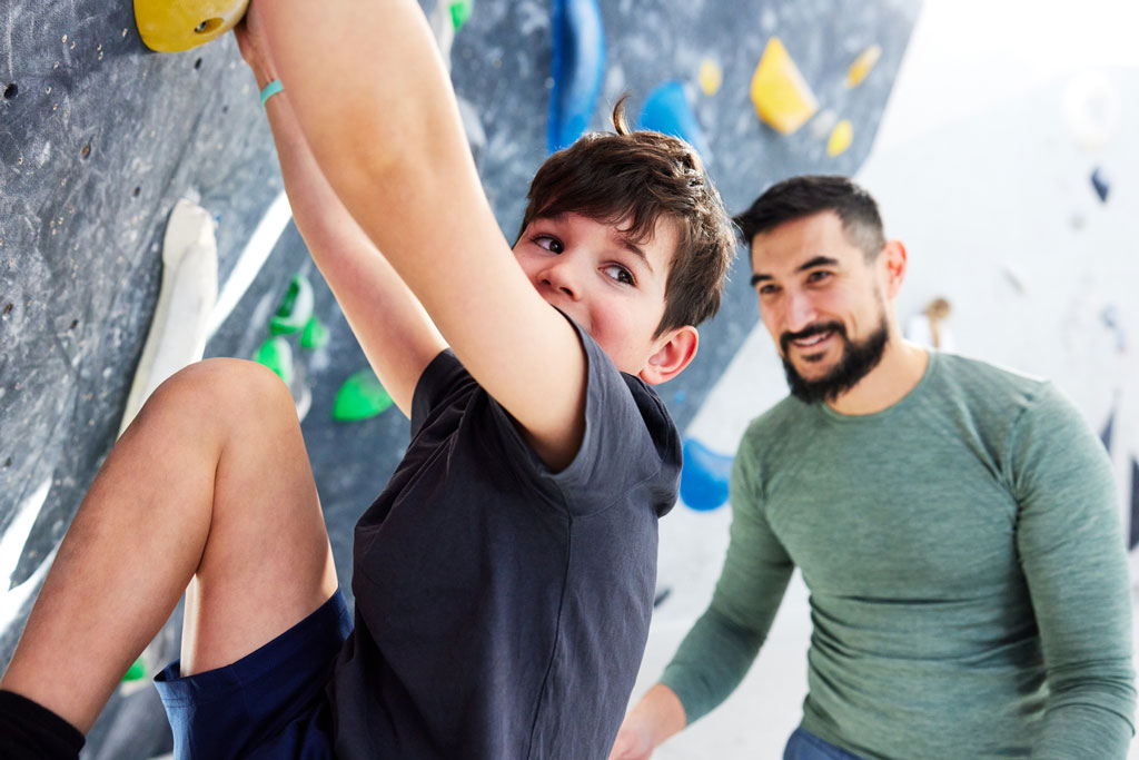 urbanapes_bouldern_kinder_2 Kind an der Boulderwand mit Vater im hintergrund.